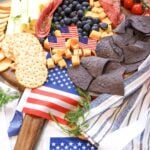 Easy 4th of July charcuterie board for cookouts with cherry tomatoes, blueberries, cheddar, swiss, salami, blue corn chips, and American flag napkins