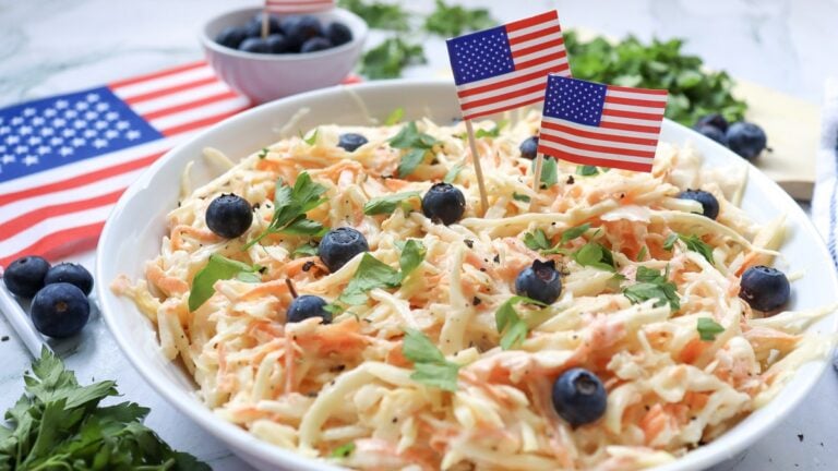 4th of July coleslaw in a white bowl topped with blueberries, parsley, and American flag picks