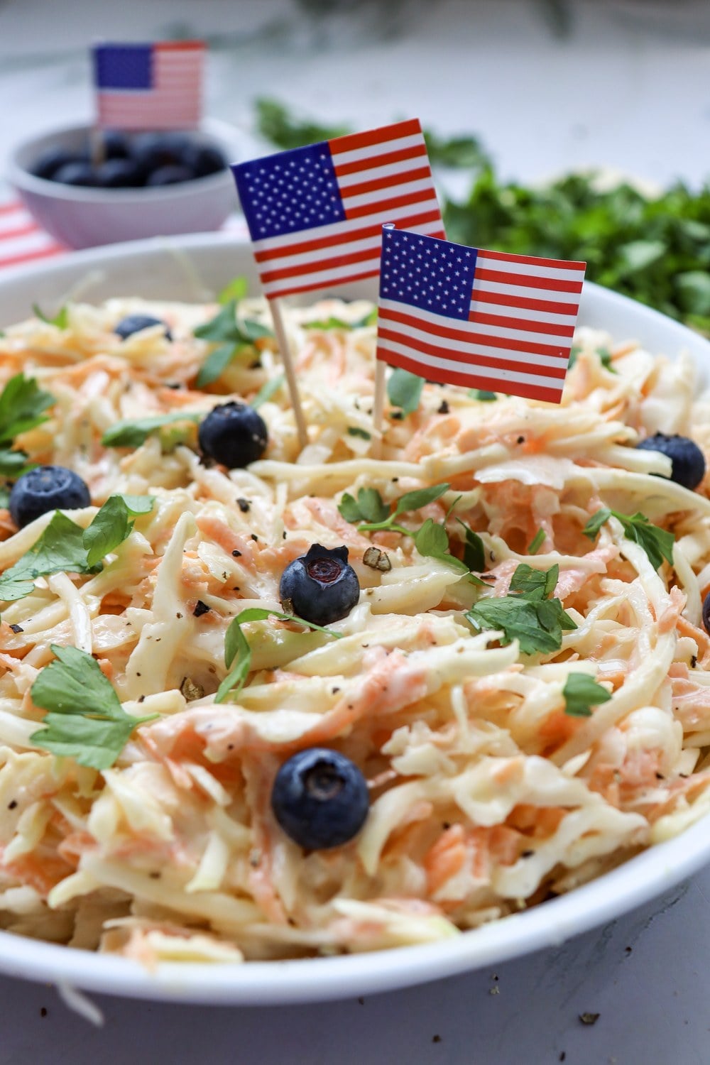 Close-up of patriotic 4th of July coleslaw topped with blueberries, parsley, and flag picks