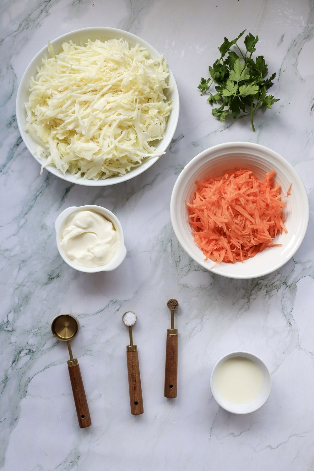 Ingredients for 4th of July coleslaw including shredded cabbage, carrots, mayonnaise, buttermilk, and parsley