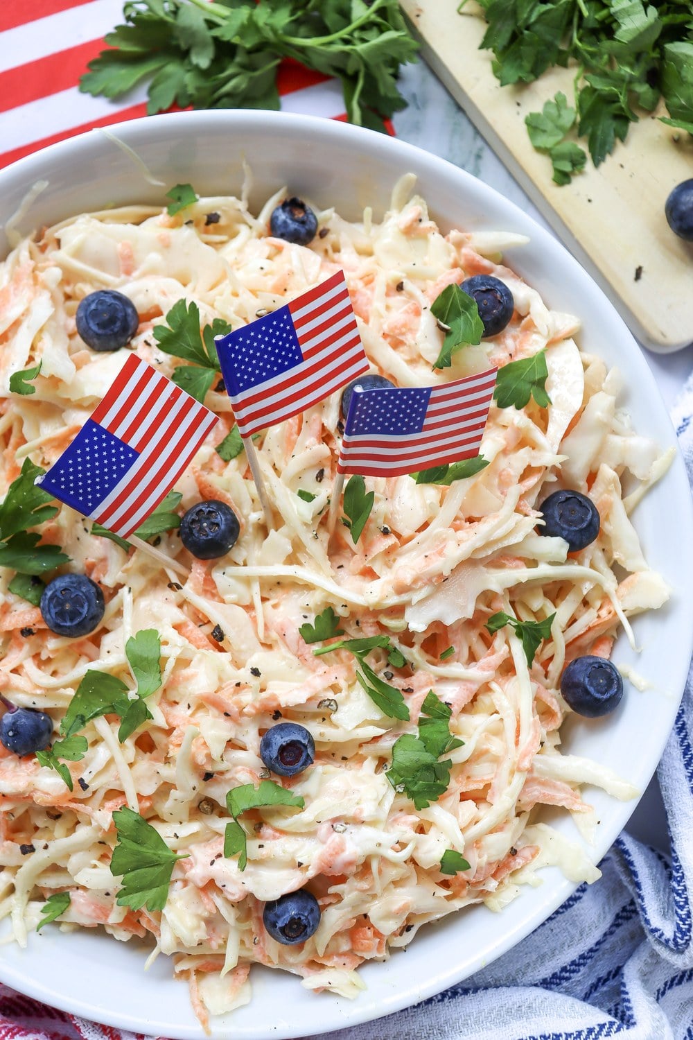 4th of July coleslaw served in a white bowl with American flag picks and blueberries