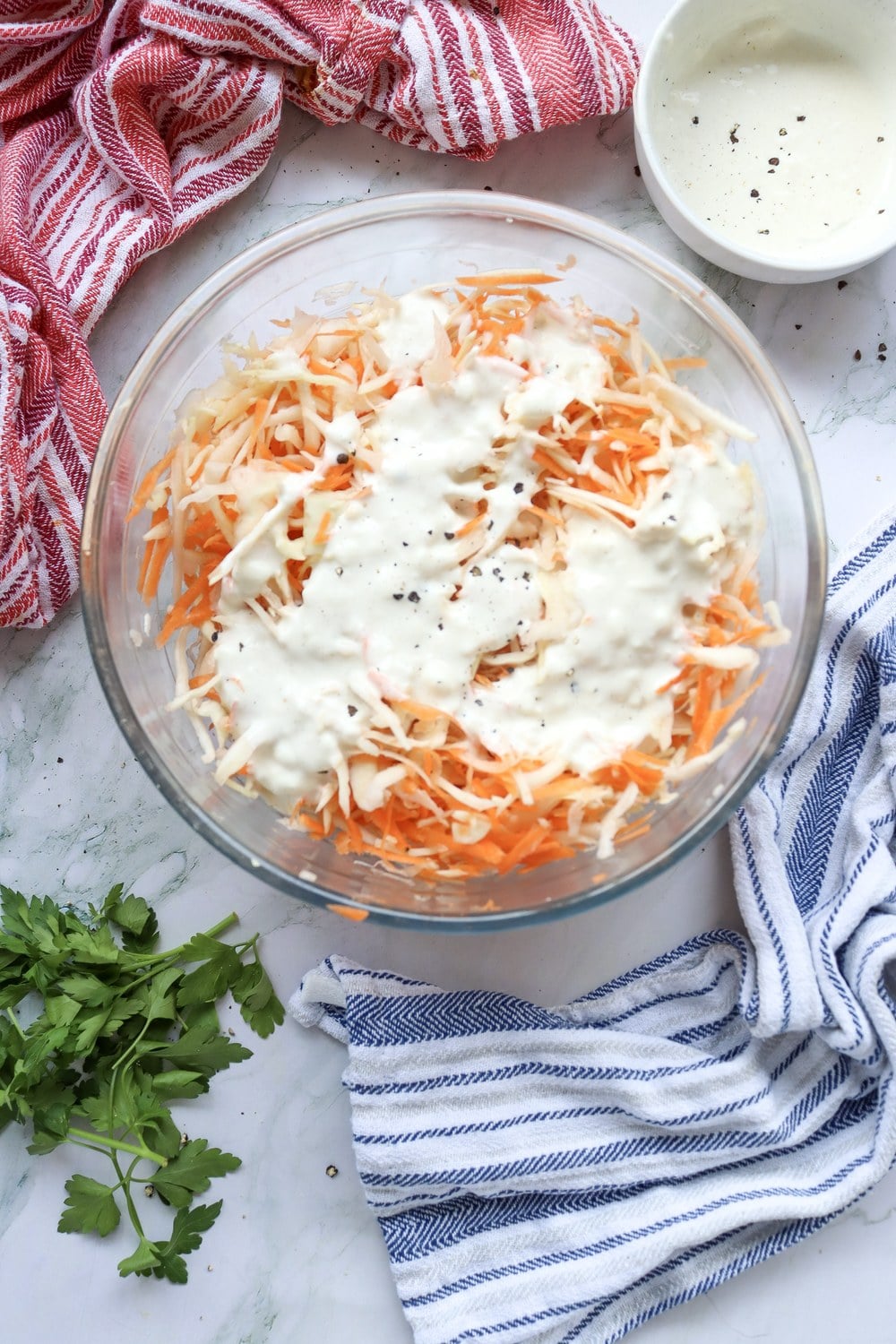 Dressing poured over shredded cabbage and carrots in a glass bowl