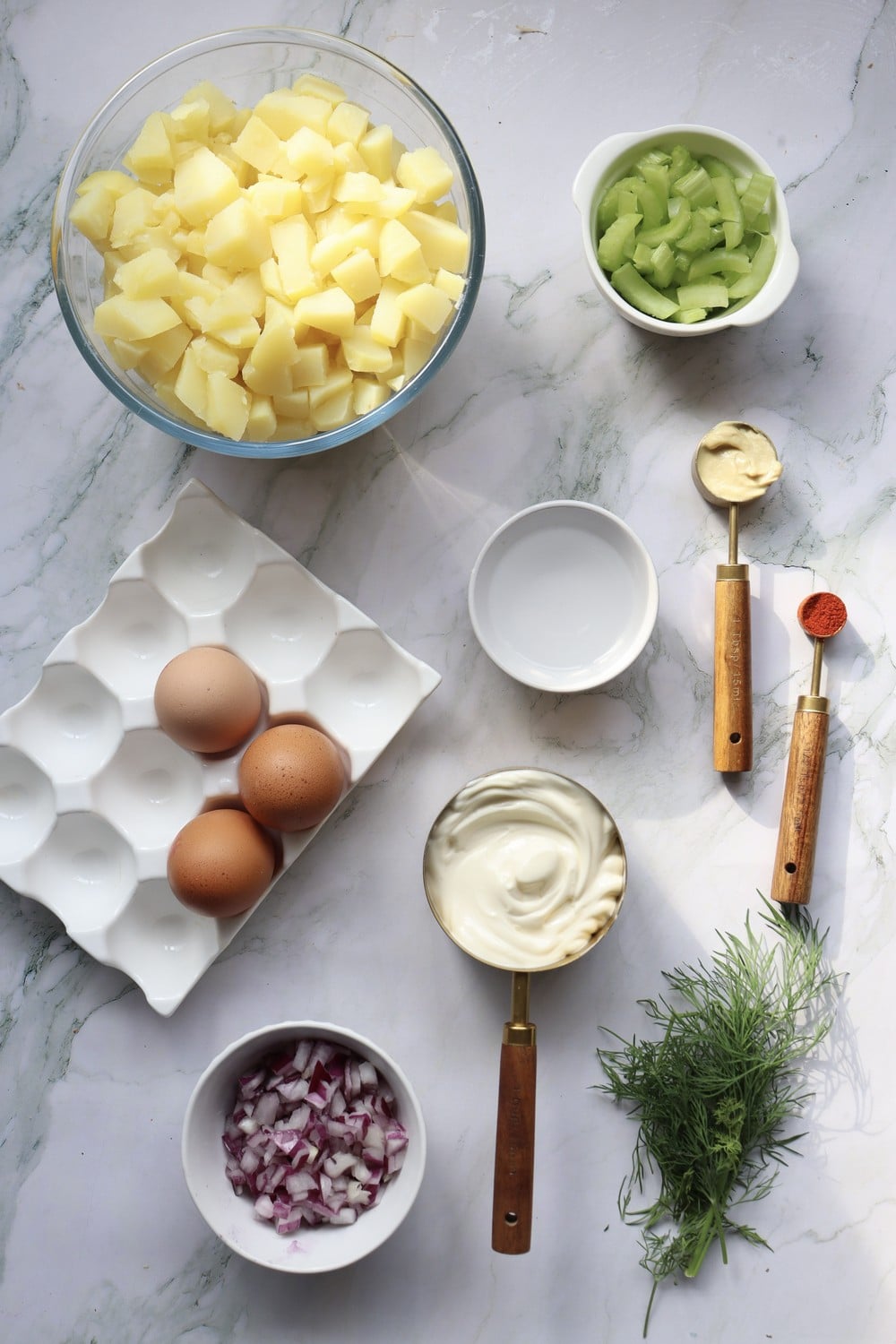 Ingredients flat lay for 4th of July potato salad: diced Yukon golds, eggs, celery, mayo, mustard, paprika, dill, and red onion