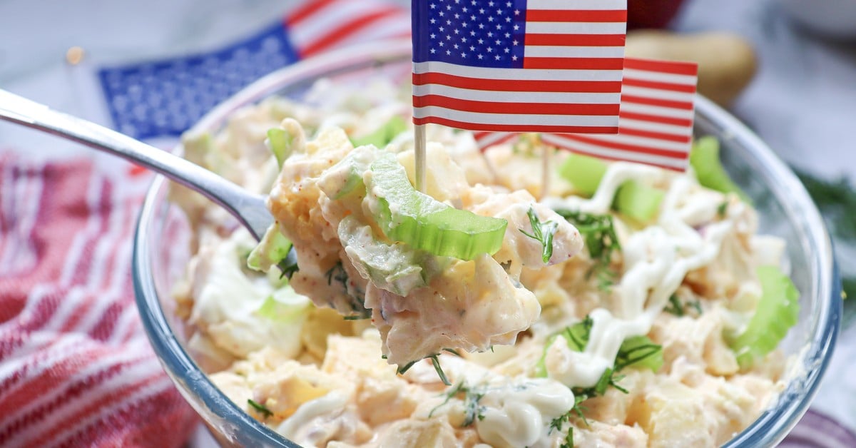 Spoonful close-up of creamy 4th of July potato salad with celery, red onion, and hard-boiled eggs visible