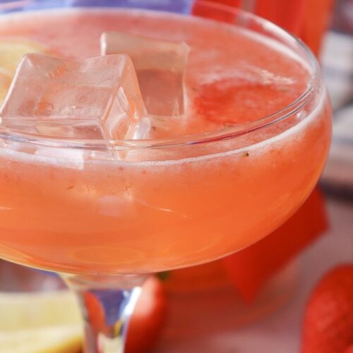 4th of July strawberry lemonade in a glass pitcher beside two ice-filled glasses with patriotic styling
