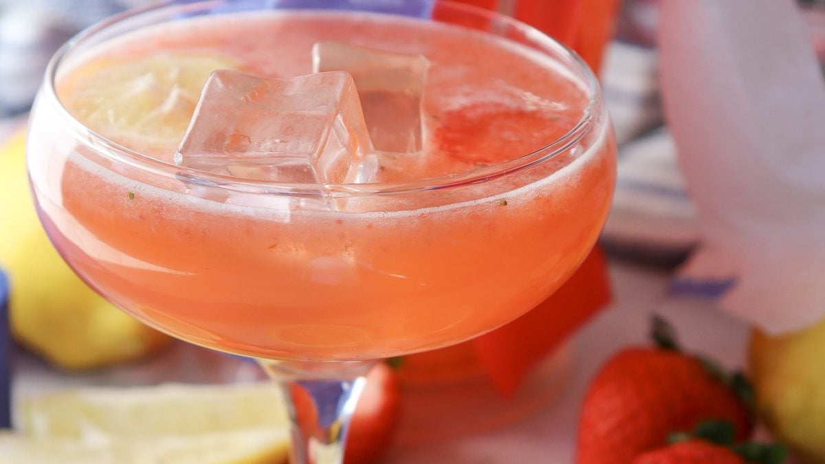 4th of July strawberry lemonade in a glass pitcher beside two ice-filled glasses with patriotic styling