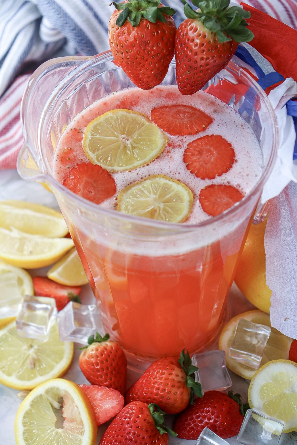 Overhead shot of a pitcher of strawberry lemonade with lemon wheels and strawberries arranged around it for 4th of July
