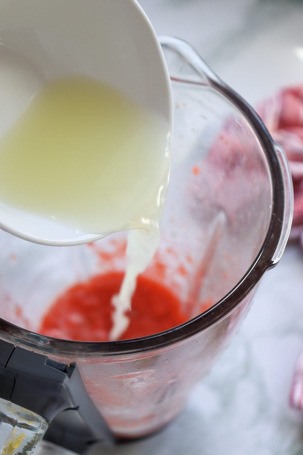 Pouring fresh lemon juice into a pitcher of strawberry puree and water for 4th of July strawberry lemonade