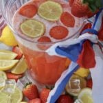 Top-down view of a glass pitcher of 4th of July strawberry lemonade with floating lemon wheels and fresh strawberries