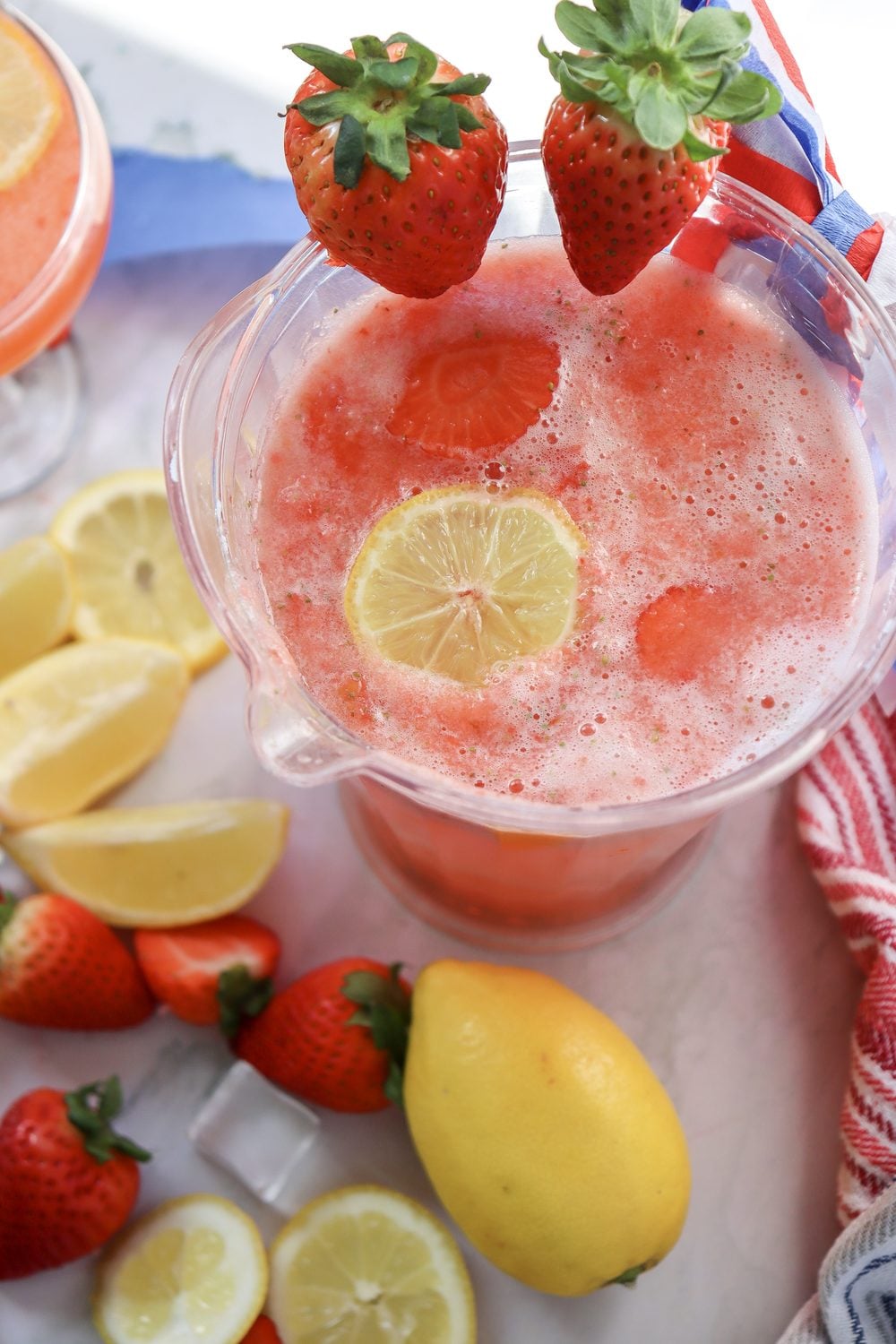 Glass pitcher of 4th of July strawberry lemonade with lemon wheels and strawberries on the side