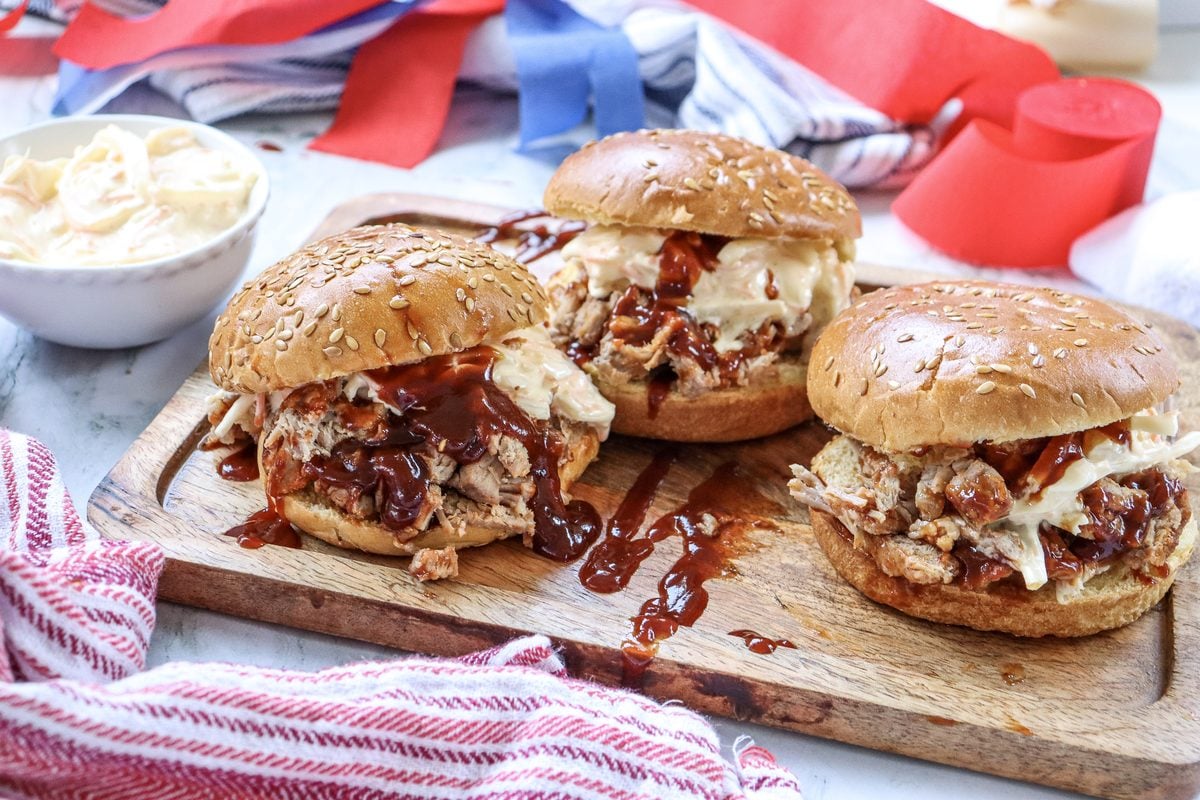 BBQ pulled pork sandwiches on a wooden board with a 4th of July red, white, and blue background, perfect for a summer cookout party.