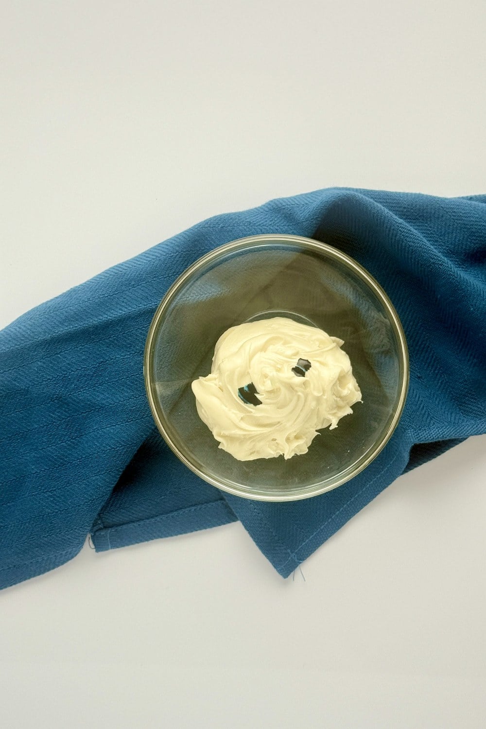 Drops of blue gel food coloring being added to a bowl of white frosting