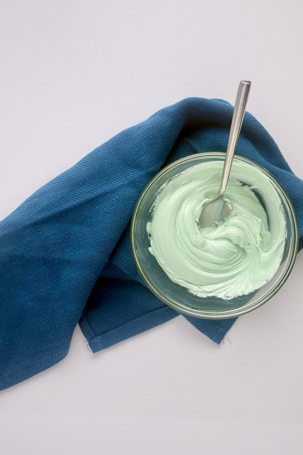 Soft teal blue frosting in a glass bowl after mixing in blue spirulina