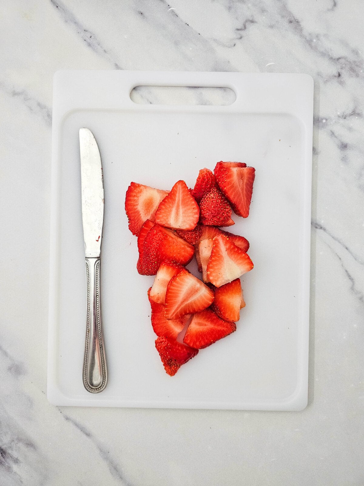 Fresh strawberries sliced on a white cutting board with a knife beside them