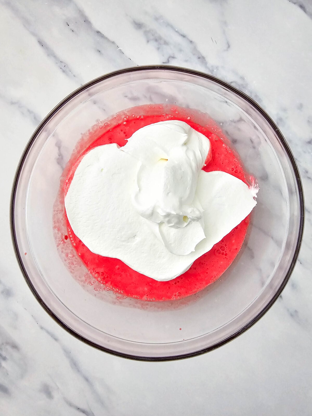 Cool Whip dolloped on top of the pink gelatin and cottage cheese mixture