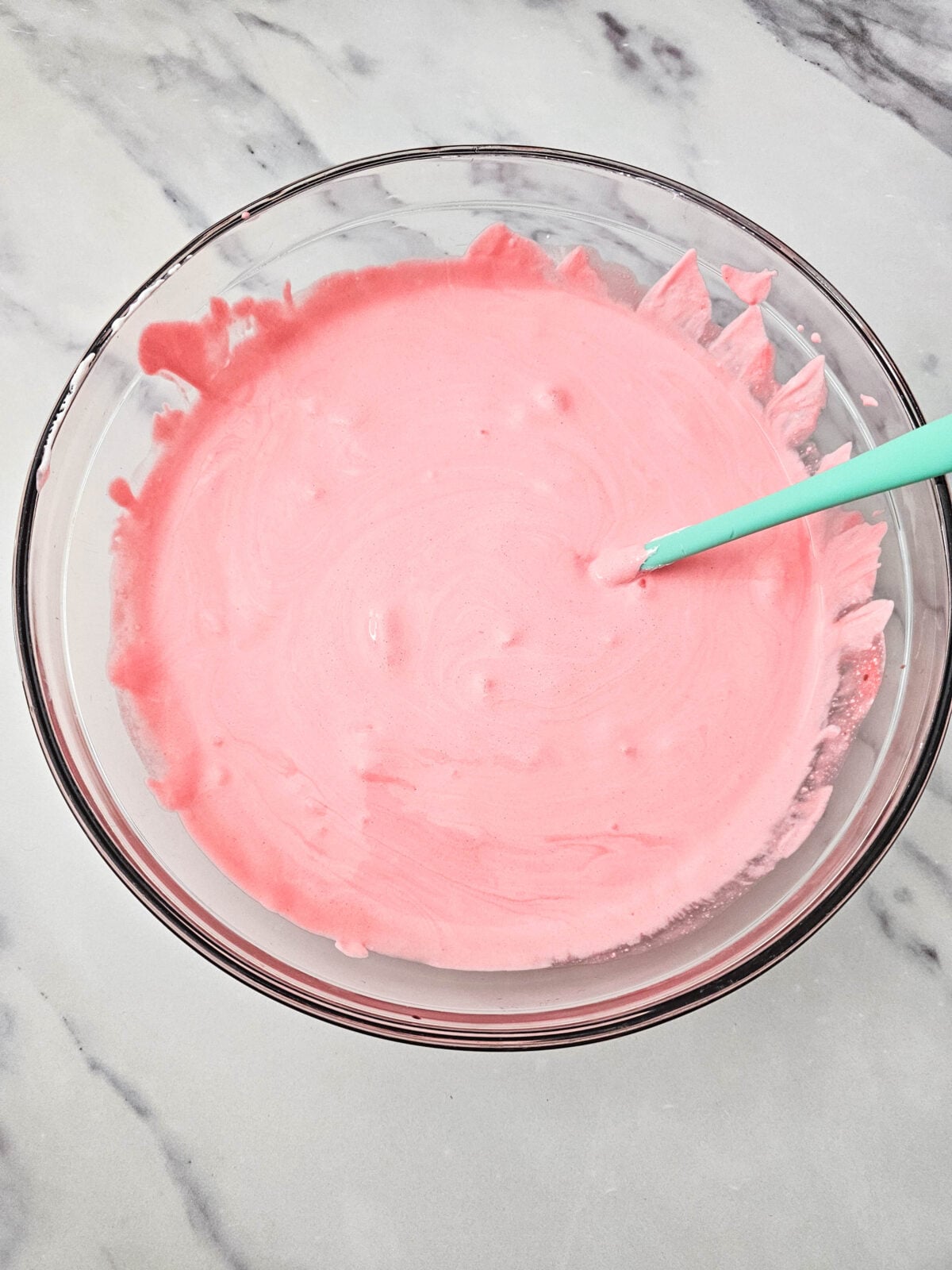 Smooth, even pink fluff mixture in a glass bowl with a teal spatula