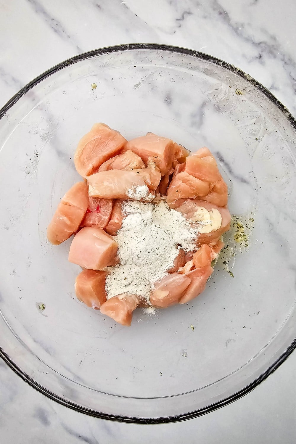 Cubed chicken breast in a glass bowl with a dry ranch seasoning packet poured on top.