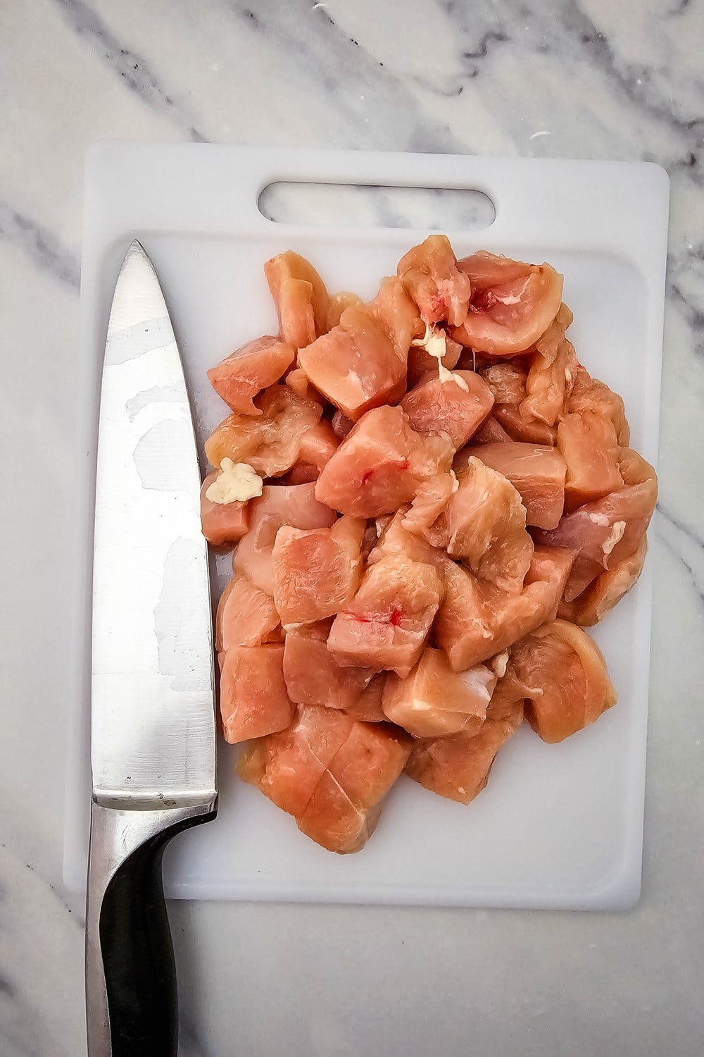 Boneless skinless chicken breast cubed into one-inch pieces on a white cutting board.