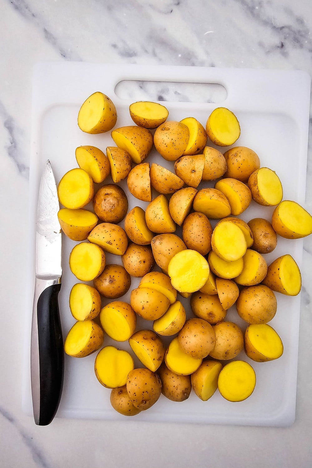 Baby potatoes halved on a white cutting board, ready for roasting.