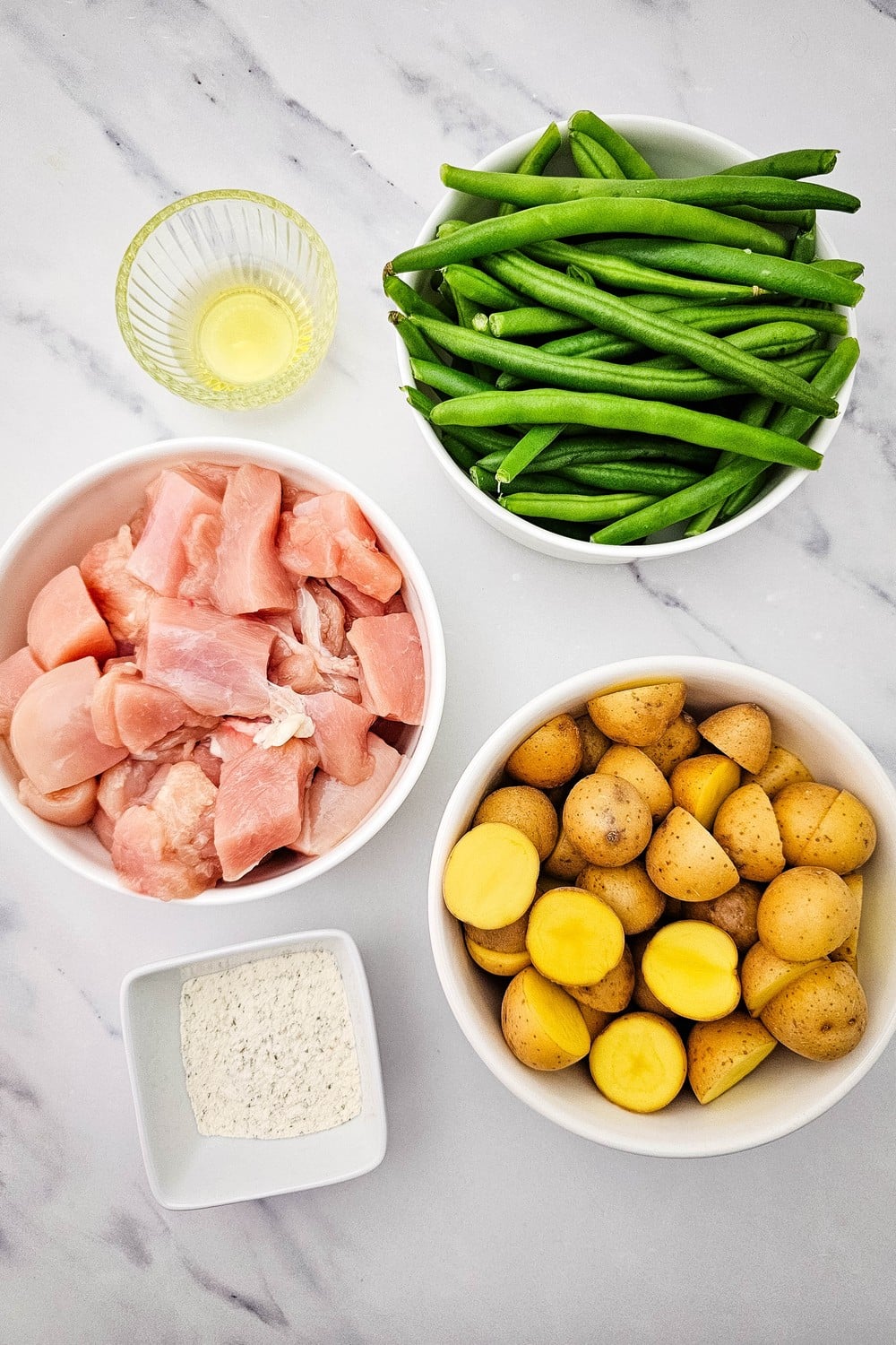 Ingredients for sheet pan ranch chicken and veggies: cubed chicken breast, halved baby potatoes, fresh green beans, olive oil, and dry ranch seasoning.