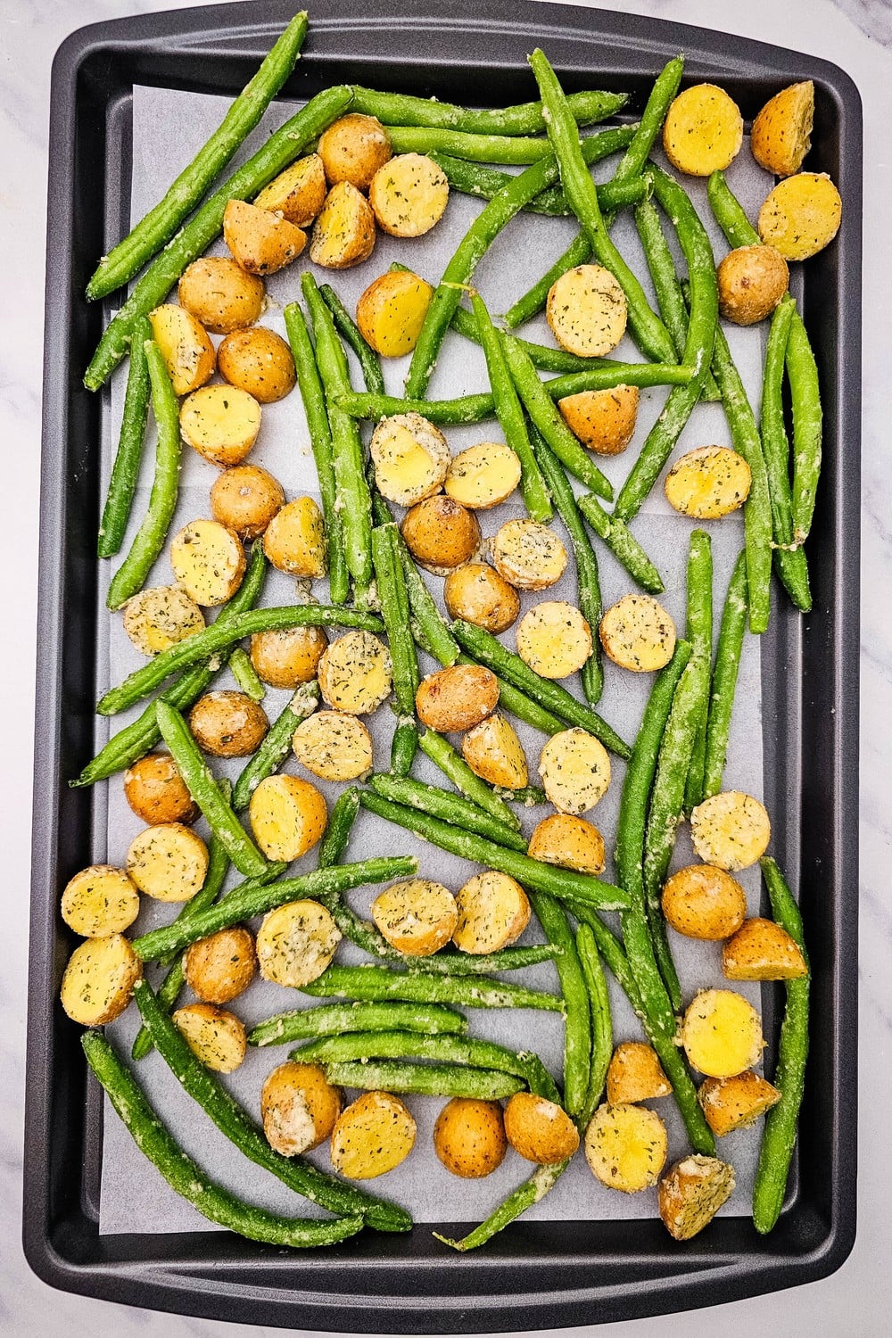 Ranch-coated potatoes and green beans spread out on a parchment-lined sheet pan.
