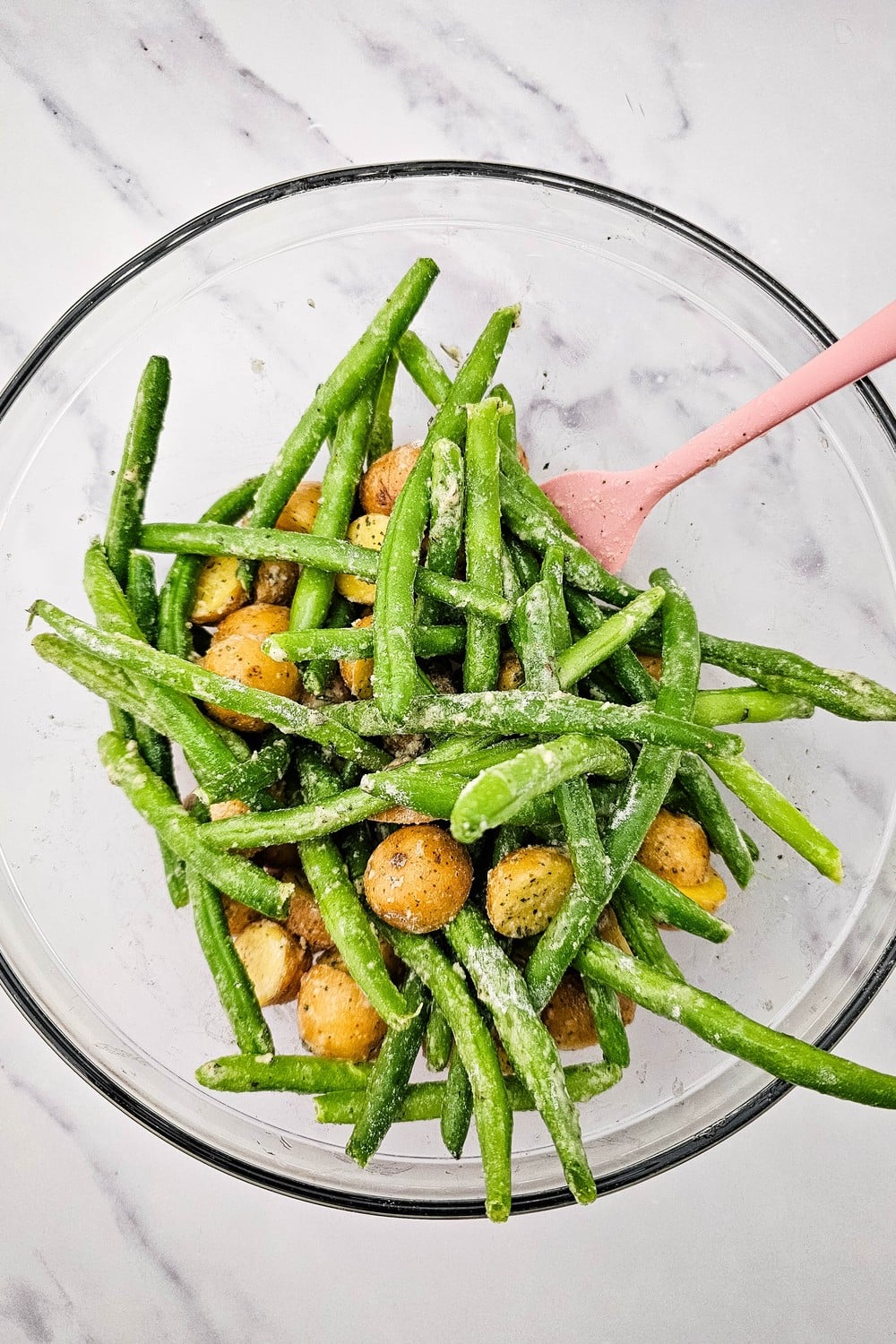 Potatoes and green beans tossed with olive oil and dry ranch seasoning in a glass bowl.