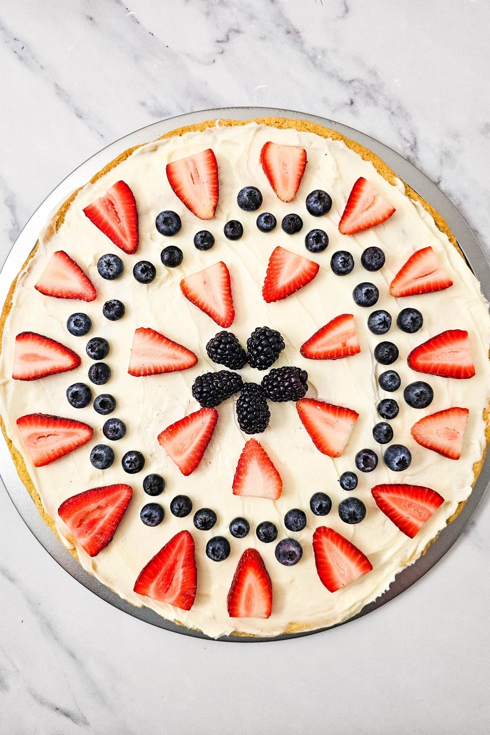 Fully assembled red, white, and blue fruit pizza with a cluster of blackberries piled in the center