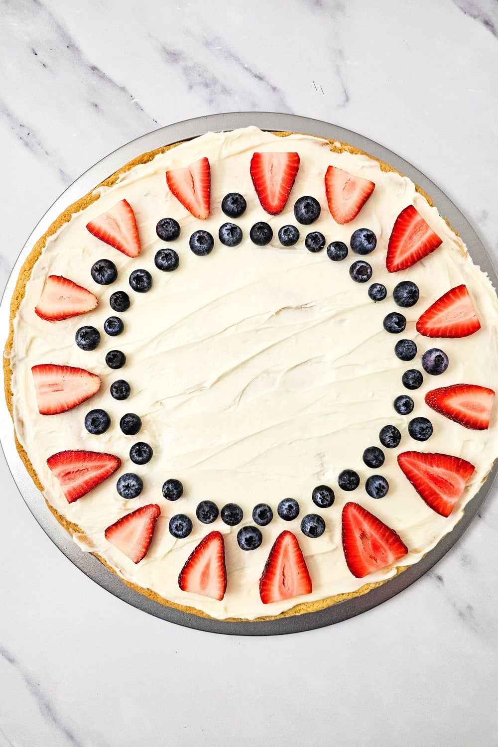 Blueberries tucked between strawberry wedges in arches and pairs on red, white, and blue fruit pizza