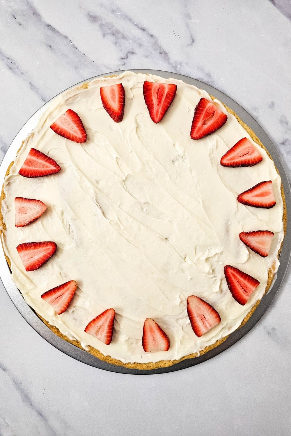 Outer ring of strawberry wedges arranged in a sunburst pattern around the edge of a frosted sugar cookie crust