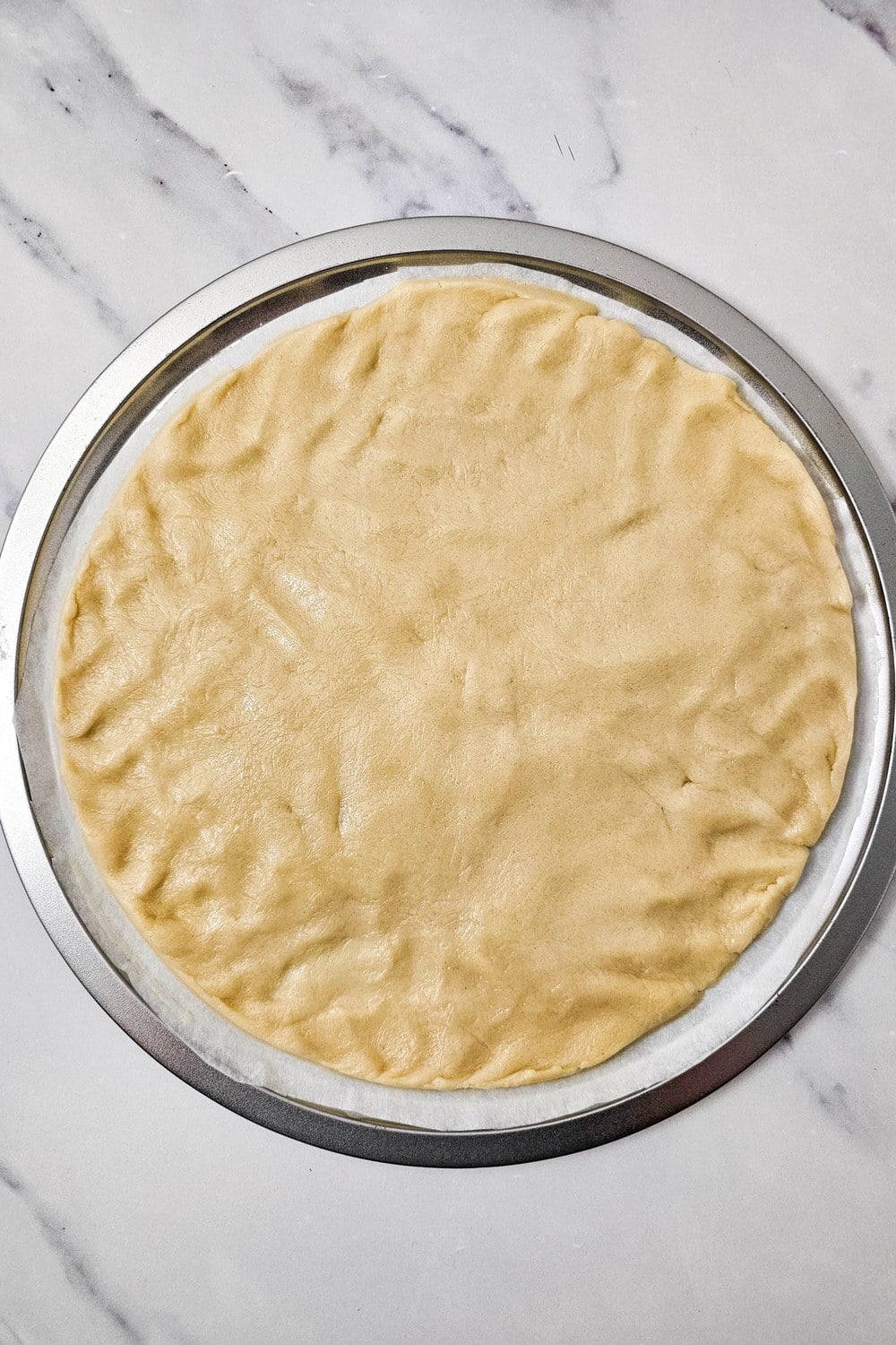 Sugar cookie dough pressed into a parchment-lined pizza pan ready to bake for red, white, and blue fruit pizza