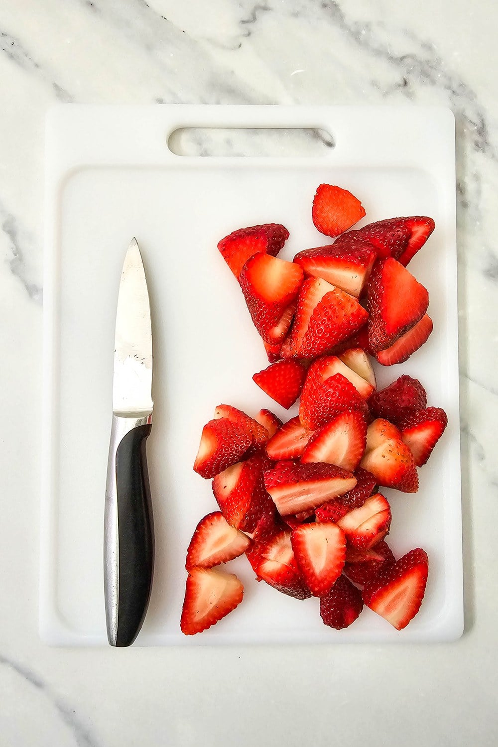 Fresh strawberries cut lengthwise into wedges on a white cutting board with a paring knife alongside