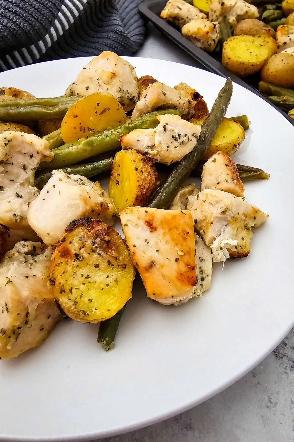 Close-up of sheet pan ranch chicken and veggies on a white plate with golden chicken cubes and crisp potato halves.