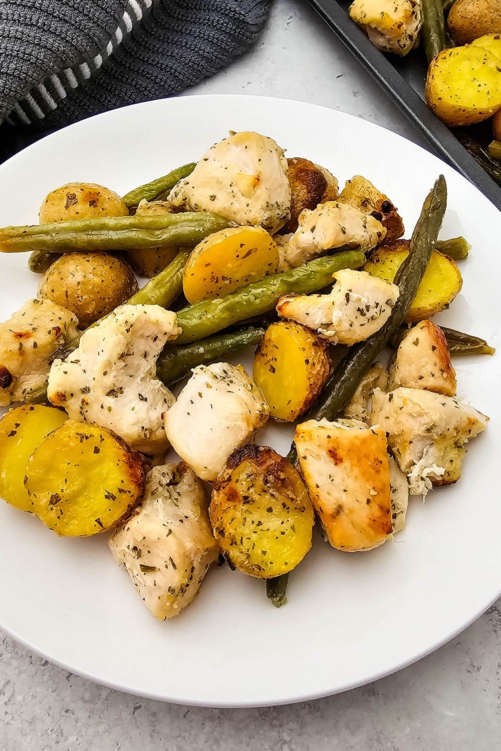 Sheet pan ranch chicken and veggies served on a white plate with the full sheet pan in the background.