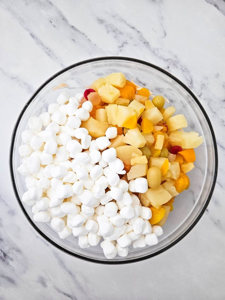 Mini marshmallows added to fruit and creamy base in a bowl
