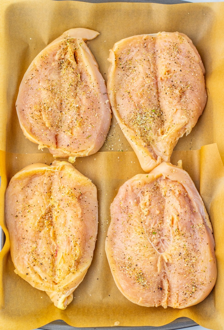 Butterflied chicken breasts seasoned on a parchment-lined baking sheet