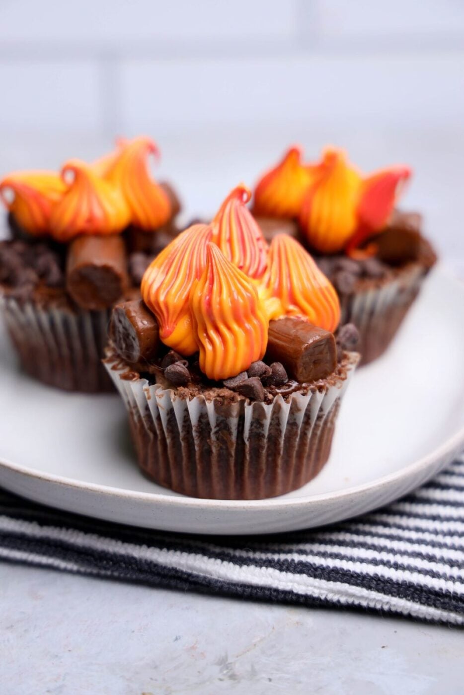 Campfire cupcakes with chocolate frosting, Tootsie Roll logs, and red, orange, and yellow buttercream flames on a white plate