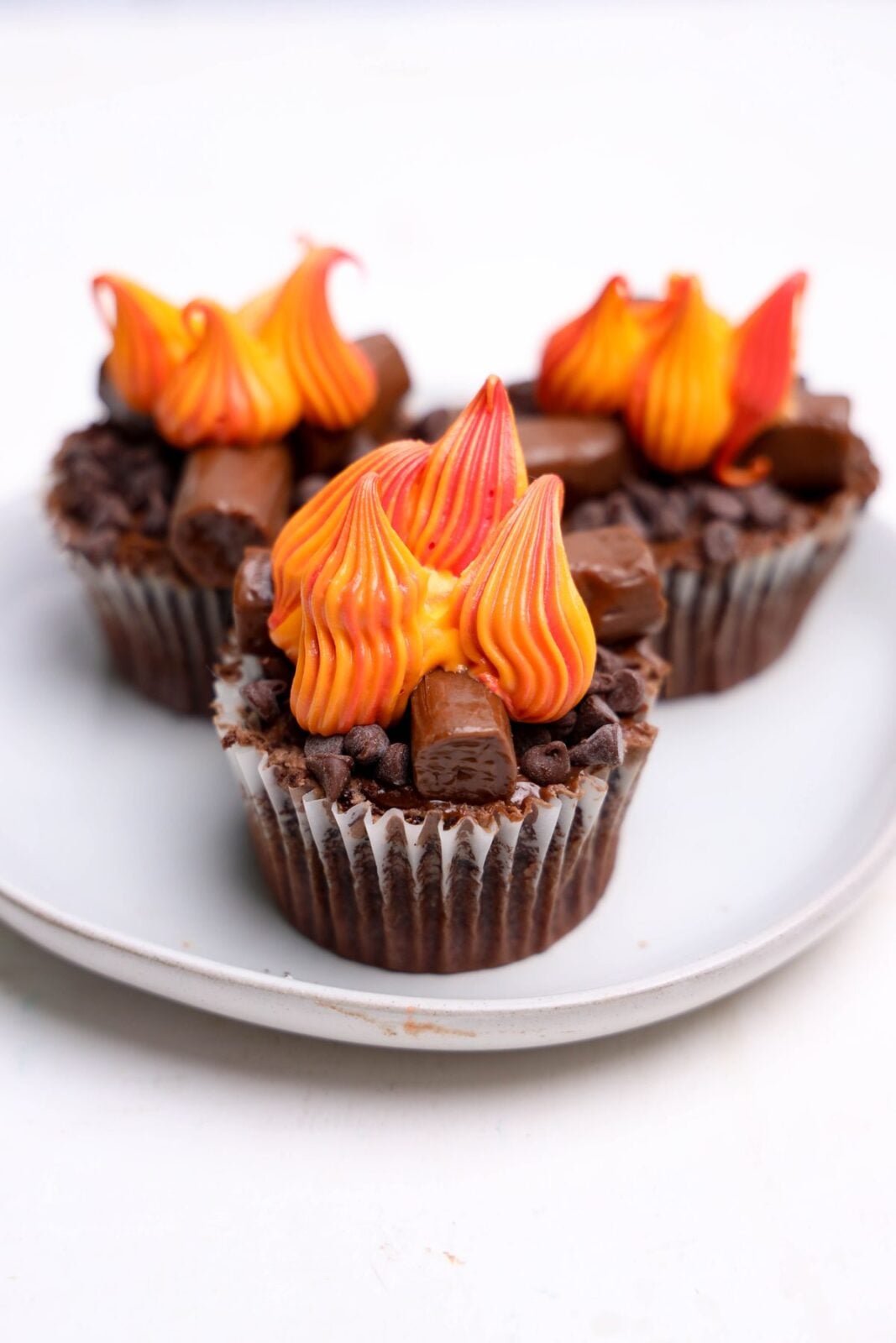Piping red, orange, and yellow buttercream flames onto campfire cupcakes