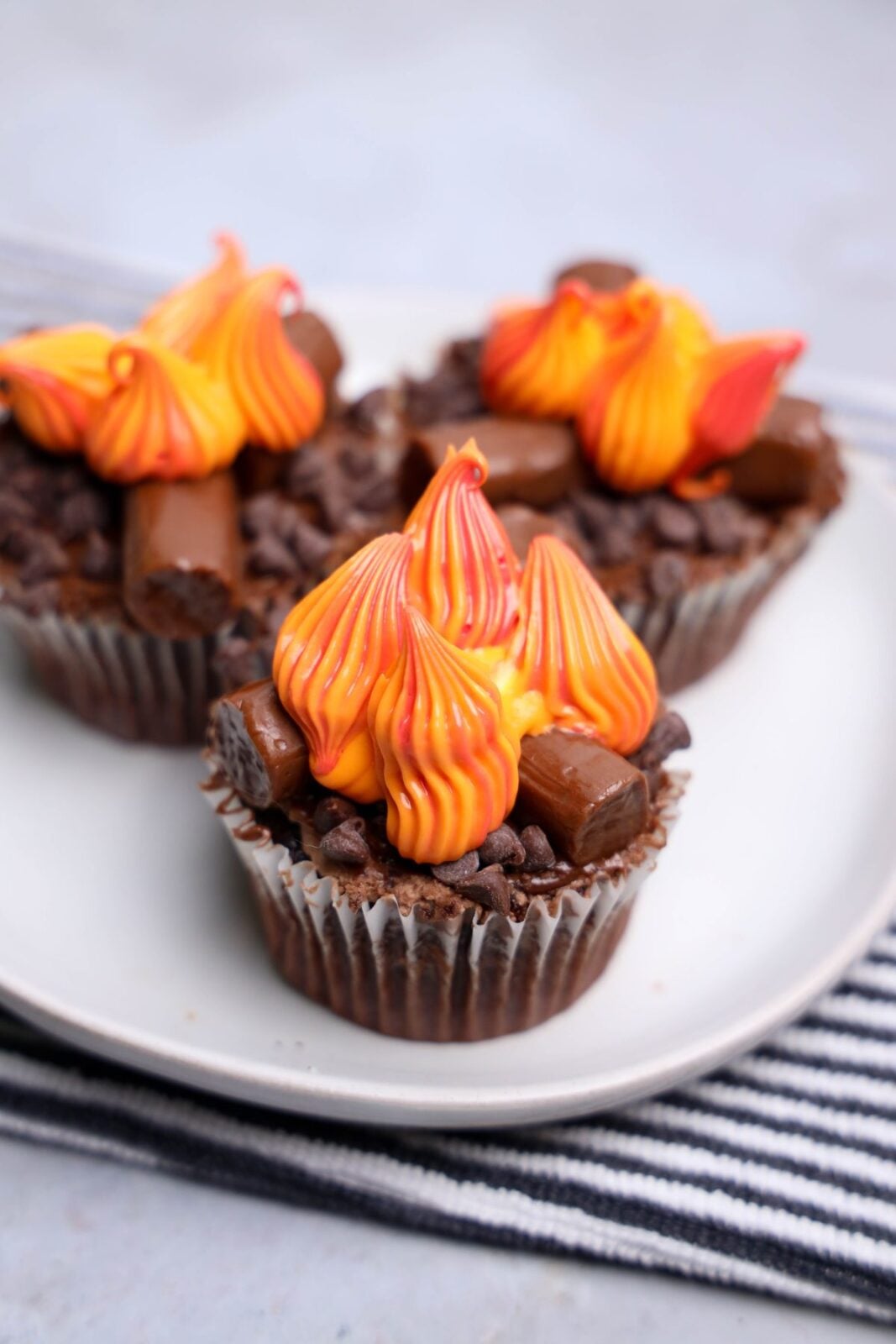 Close-up of a campfire cupcake with piped buttercream flames over chocolate Tootsie Roll logs