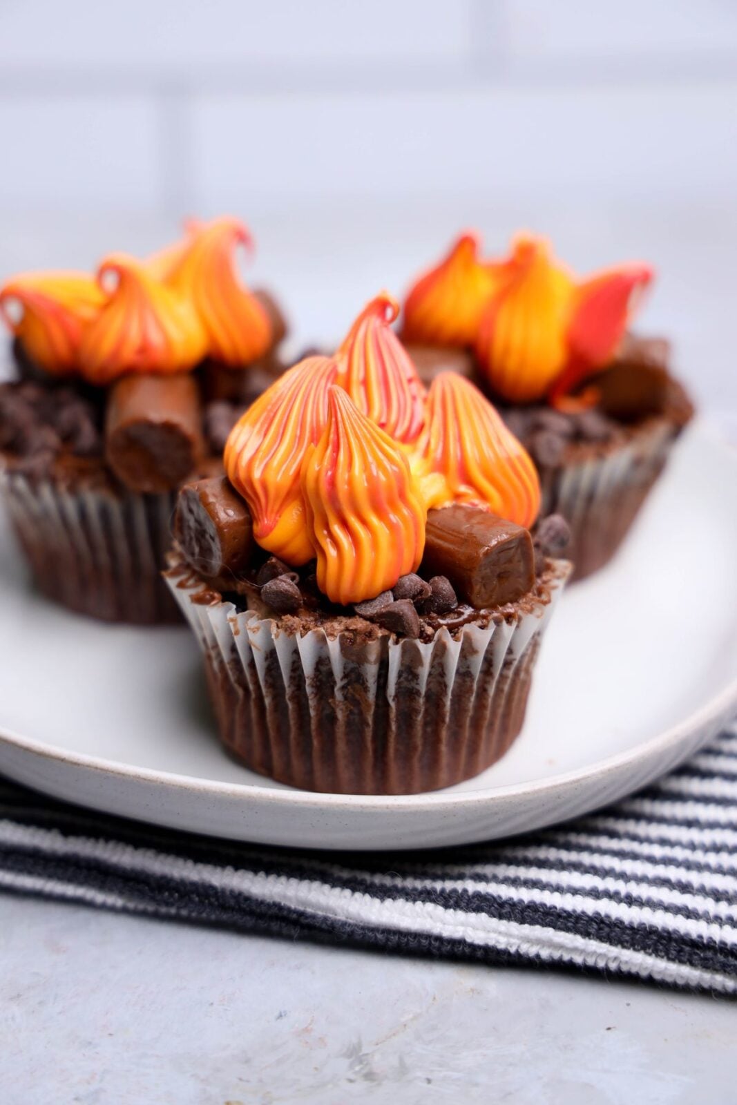 Campfire cupcakes with chocolate frosting, Tootsie Roll logs, and red, orange, and yellow buttercream flames on a white plate