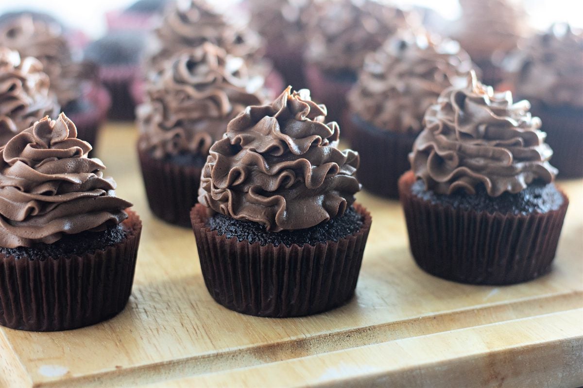 Piping chocolate buttercream onto cooled chocolate cupcakes