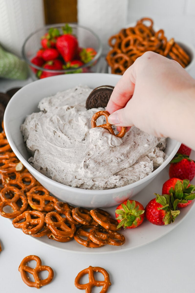 Hand dipping a pretzel into Oreo dip