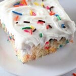Funfetti crazy cake slice with white frosting and rainbow sprinkles on a plate