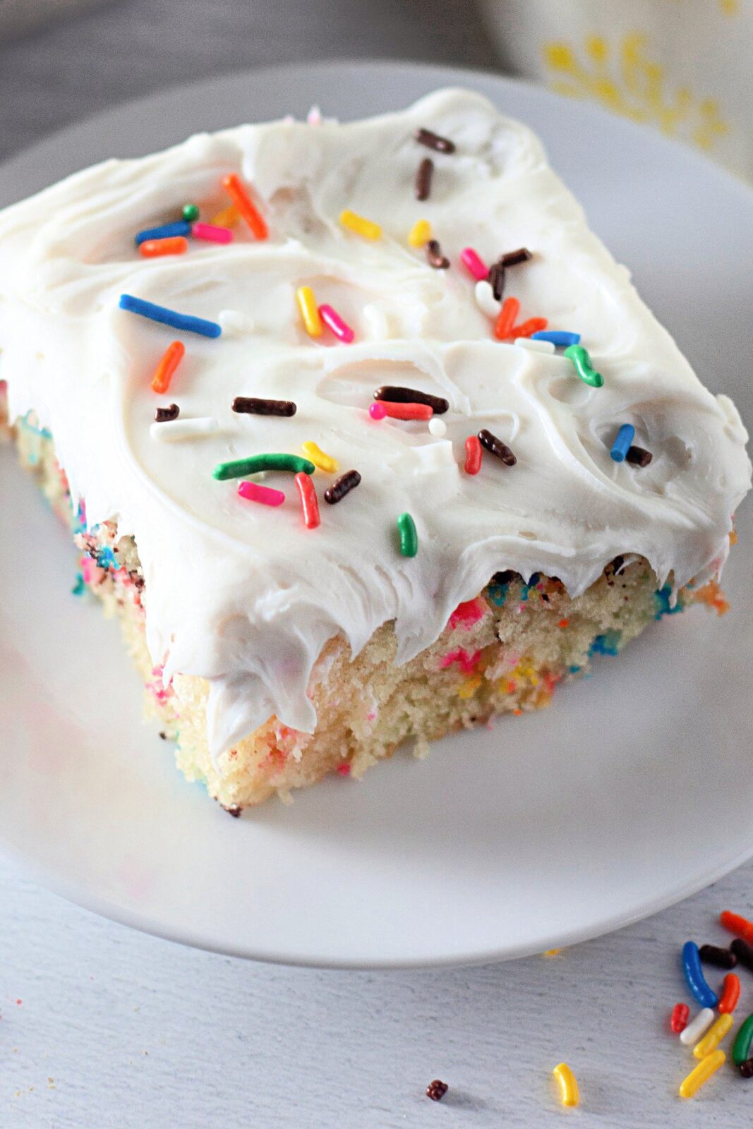 Funfetti crazy cake slice with white frosting and rainbow sprinkles on a plate