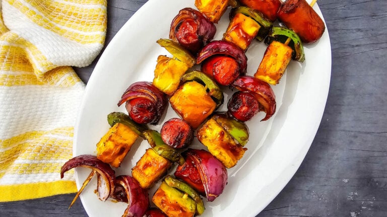 Grilled hot dog kabobs on a white platter with barbecue sauce