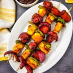 Grilled hot dog kabobs served on a platter with barbecue sauce
