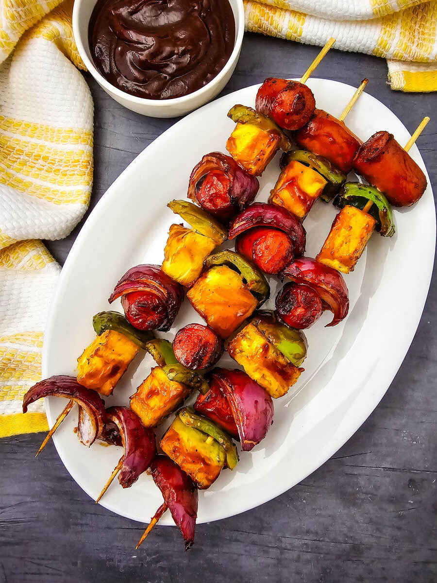 Grilled hot dog kabobs served on a platter with barbecue sauce
