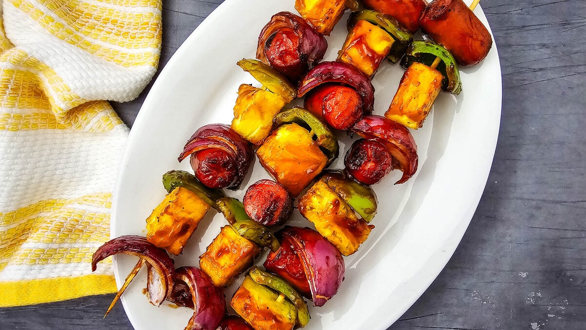Grilled hot dog kabobs on a white platter with barbecue sauce