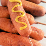 Homemade corn dogs on wooden sticks with mustard
