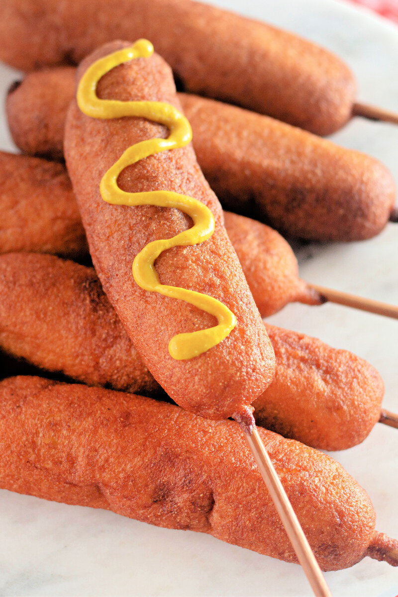 Homemade corn dogs on wooden sticks with mustard