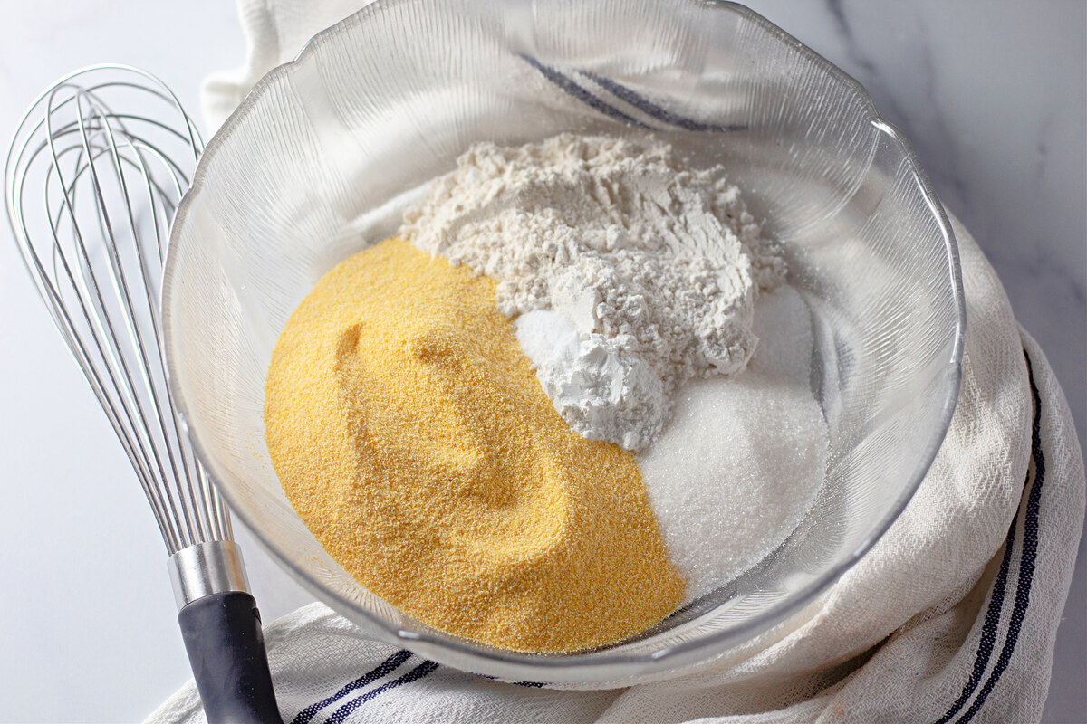 Dry corn dog batter ingredients in a glass mixing bowl
